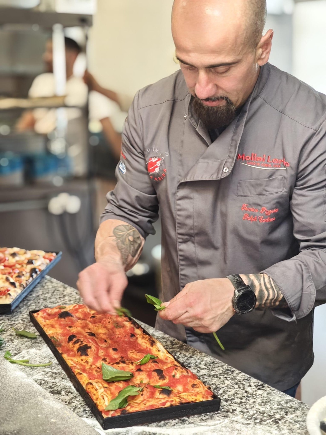 Ralph Carlone holding a freshly baked pizza in front of a wood-fired oven